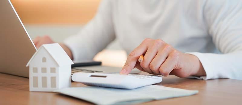 Person on computer with calculator and house figurine